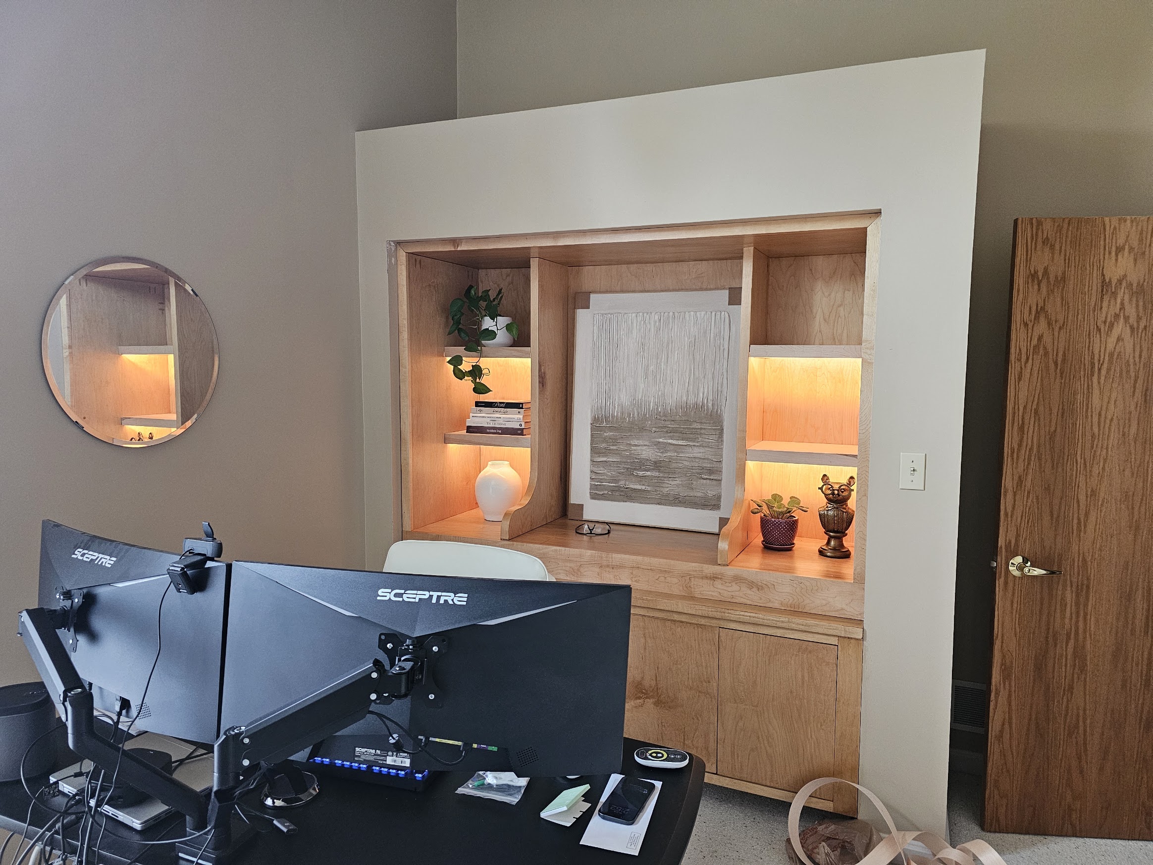 Wider view of the home office showing the desk, monitors, and the lit built-in behind